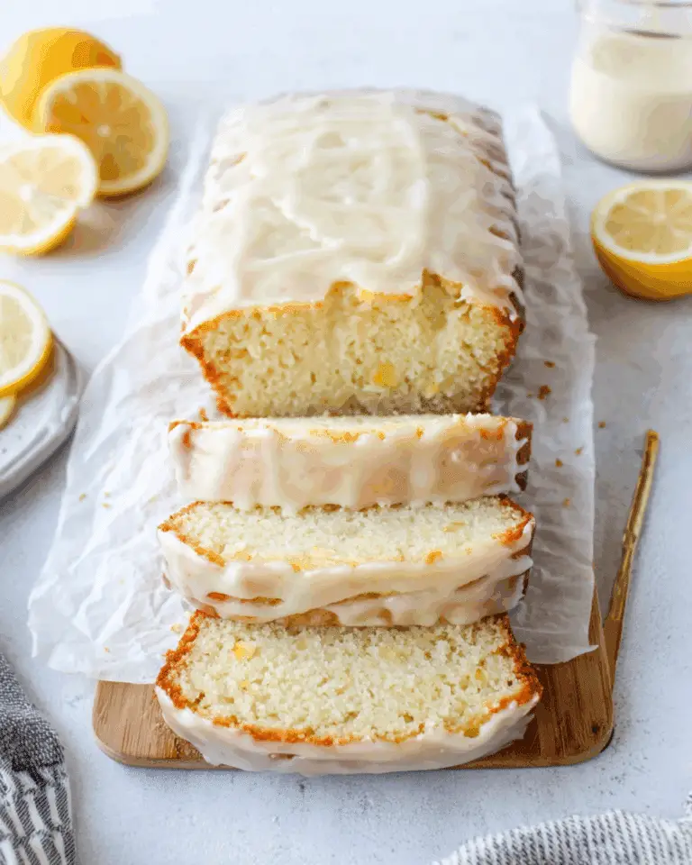 Greek Yogurt Lemon Loaf with a glossy lemon glaze, sliced and displayed on a wooden board with fresh lemon halves.
