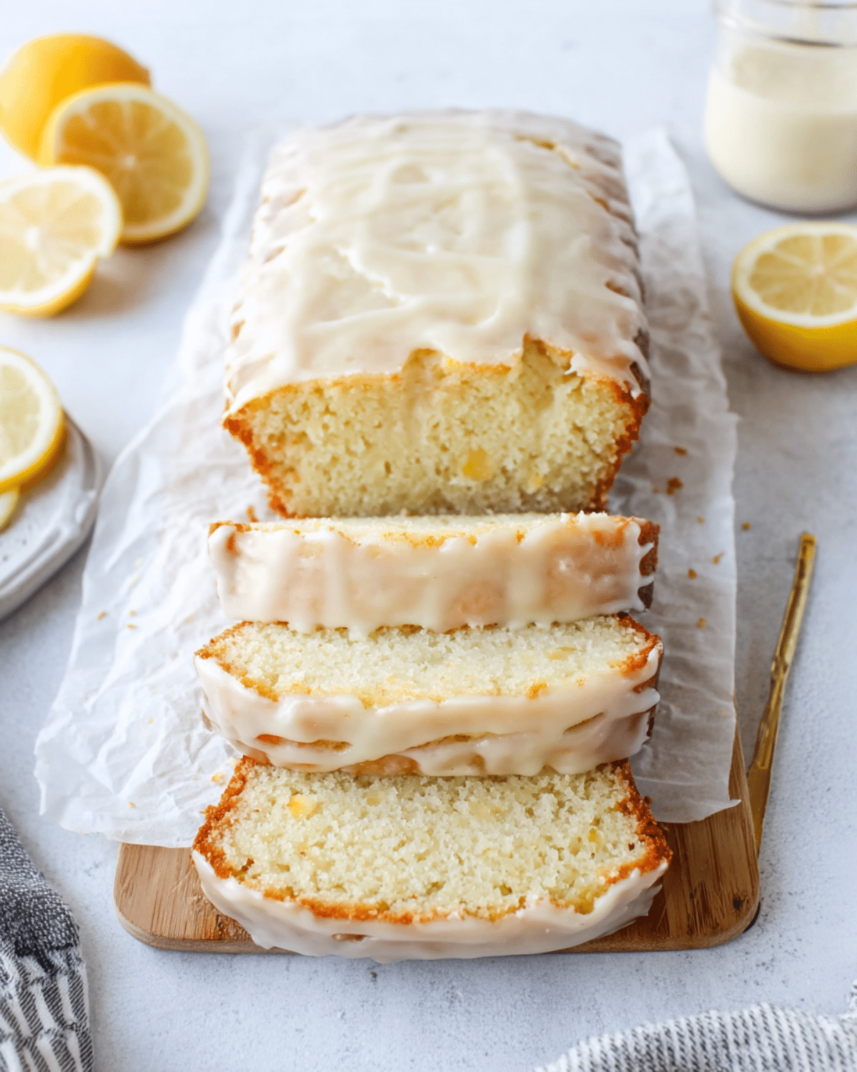 Greek Yogurt Lemon Loaf with a glossy lemon glaze, sliced and displayed on a wooden board with fresh lemon halves.