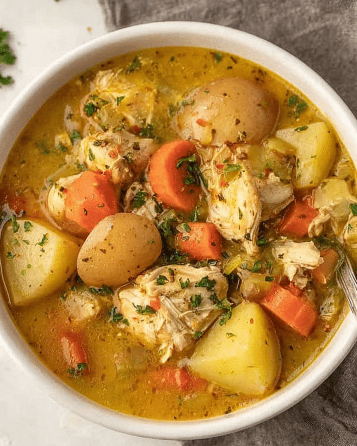 A bowl of hearty chicken stew filled with chunks of chicken, potatoes, carrots, and herbs in a savory broth.