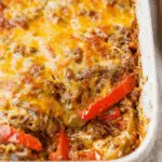 Hearty stuffed pepper casserole with melted cheese, ground beef, rice, and red bell peppers baked in a white dish.
