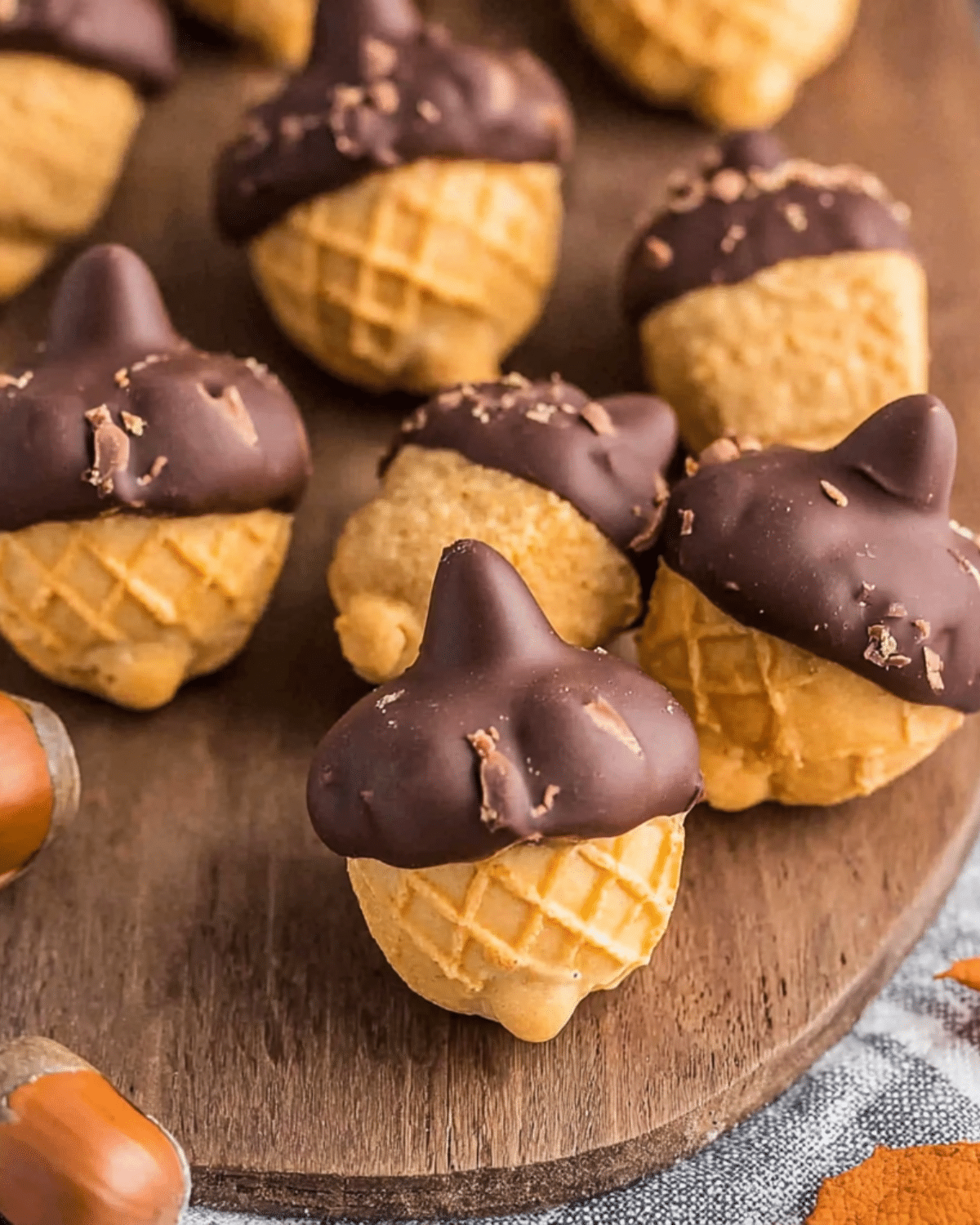Close-up of Hershey Kiss Acorn Treats made with cookies, chocolate frosting, and Hershey's Kisses on a wooden surface.