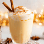 Holiday Jamaican Eggnog Recipe topped with whipped cream, cinnamon, and garnished with cinnamon sticks in a clear glass.
