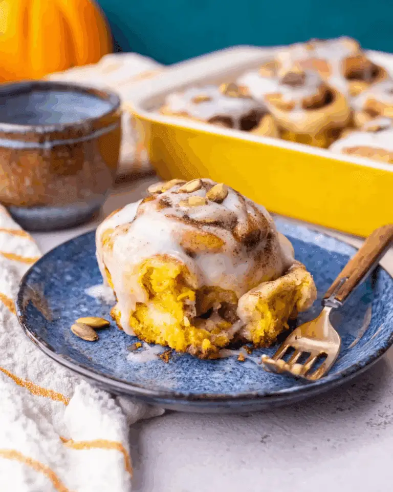 Homemade pumpkin chai cinnamon roll topped with icing and pumpkin seeds on a blue plate with a fork.