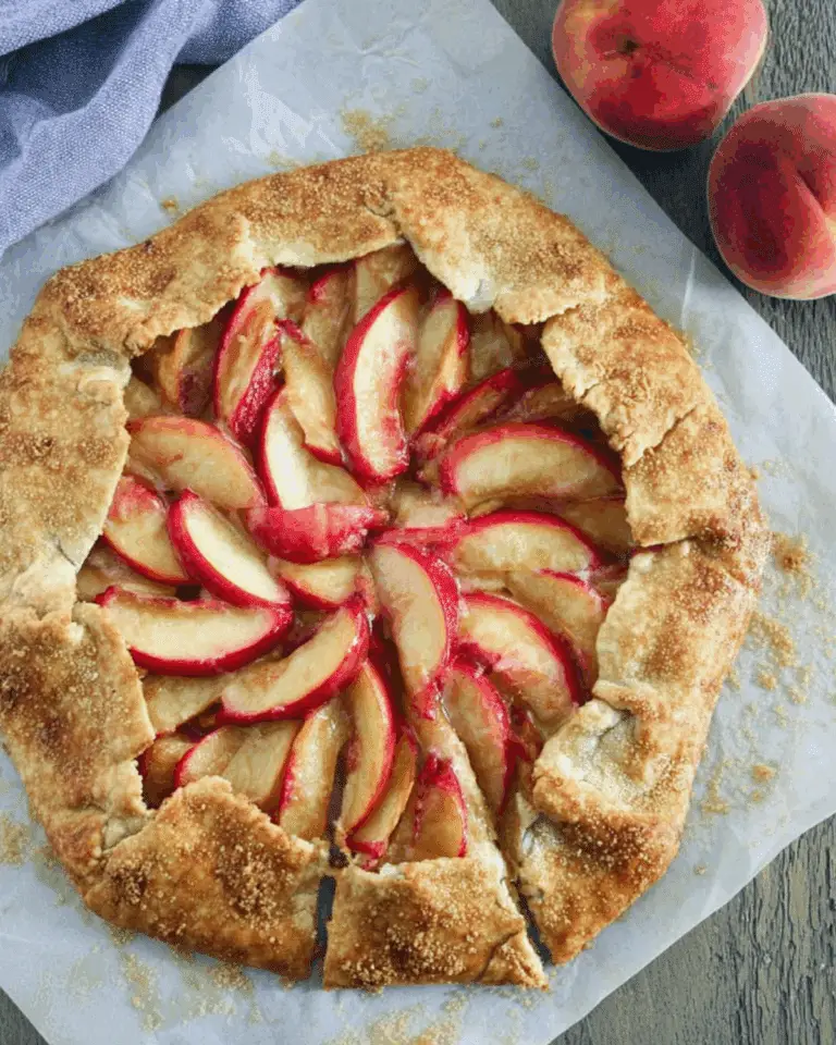 A rustic honey peach galette with golden-brown crust and beautifully arranged peach slices on parchment paper.