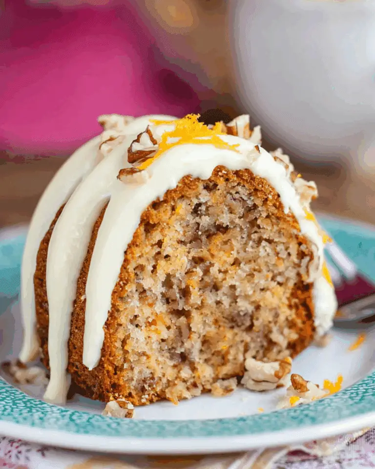 Slice of hummingbird bundt cake topped with cream cheese frosting, chopped pecans, and orange zest on a decorative plate.