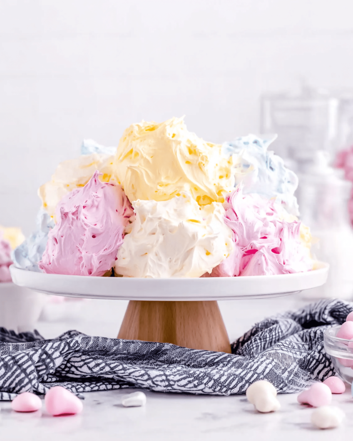 A colorful Jello Divinity Recipe dessert displayed on a white cake stand, featuring fluffy pastel swirls in pink, yellow, blue, and white.