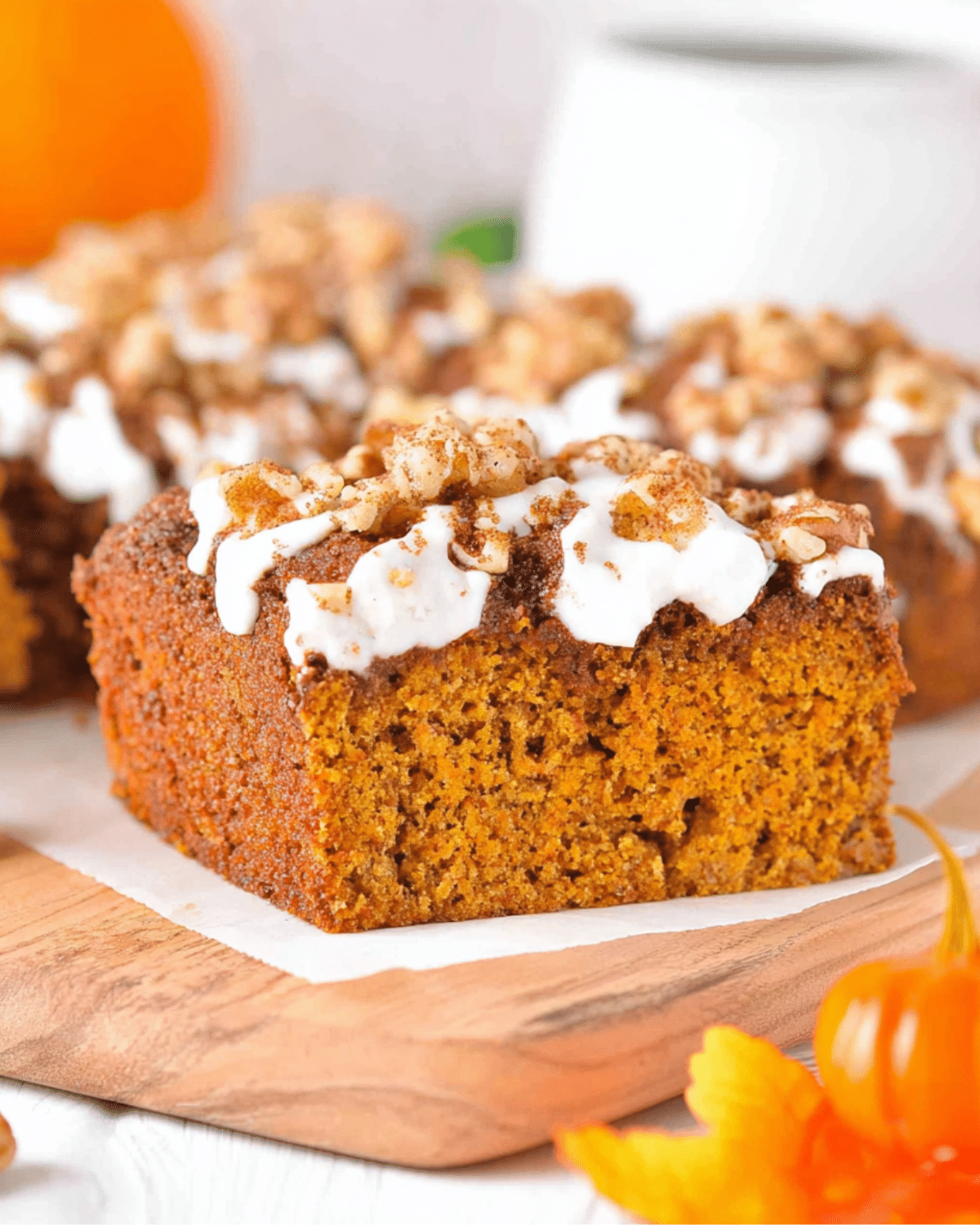 A slice of keto pumpkin cake topped with white frosting, chopped nuts, and cinnamon on a wooden board.
