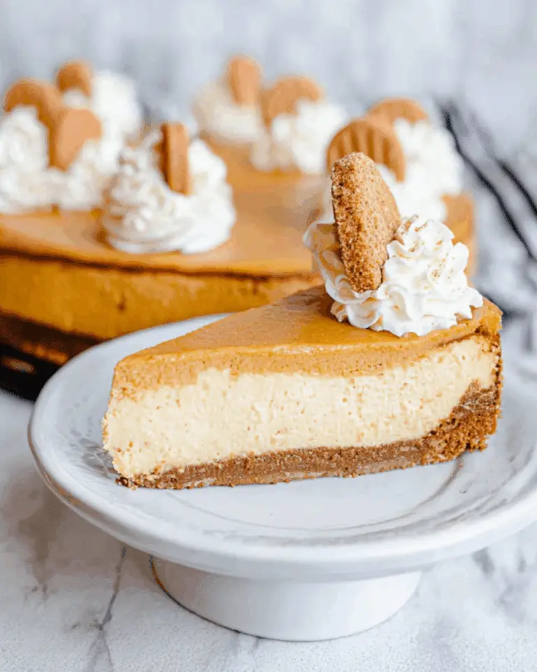 Slice of layered pumpkin cheesecake topped with whipped cream and a gingersnap cookie, with the whole cheesecake in the background.