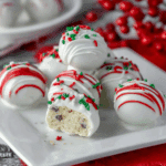 A plate of Little Debbie Christmas Tree Cake Balls coated in white chocolate, drizzled with red icing, and topped with festive sprinkles.