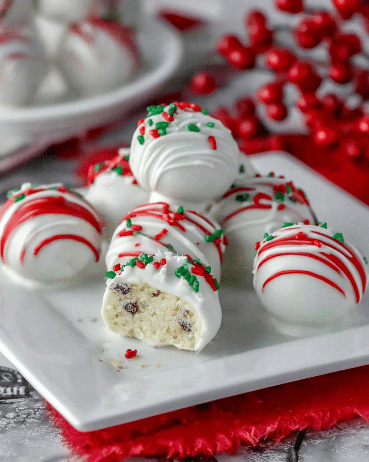 A plate of Little Debbie Christmas Tree Cake Balls coated in white chocolate, drizzled with red icing, and topped with festive sprinkles.
