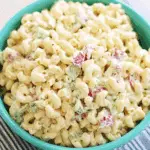 A bowl of creamy macaroni salad with elbow pasta, diced red peppers, and green vegetables.