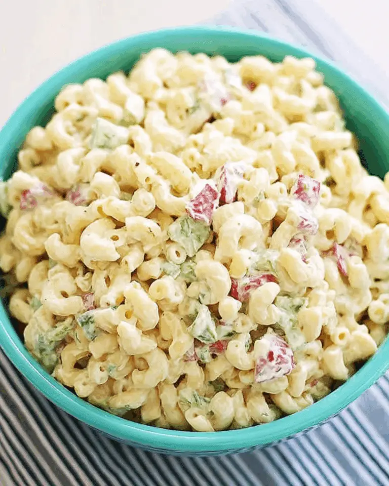 A bowl of creamy macaroni salad with elbow pasta, diced red peppers, and green vegetables.