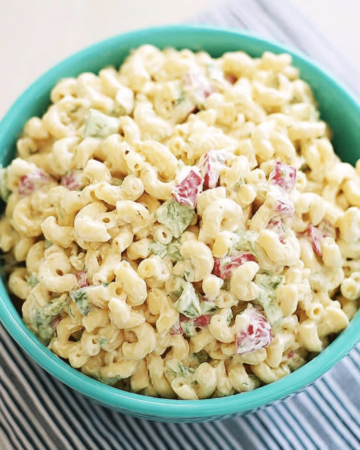 A bowl of creamy macaroni salad with elbow pasta, diced red peppers, and green vegetables.