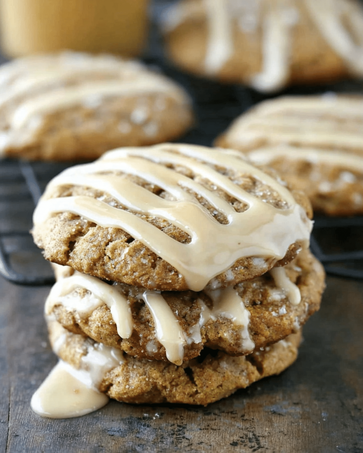 Stack of maple pumpkin cookies drizzled with a sweet maple glaze, cooling on a rustic wooden surface.