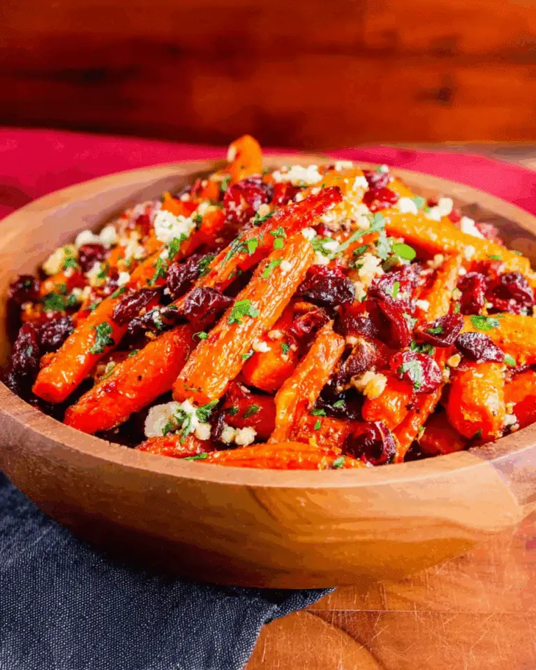 Wooden bowl filled with maple roasted carrots, cranberries, crumbled cheese, and fresh herbs.