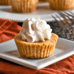 Mini keto pumpkin pie topped with a swirl of whipped cream and a sprinkle of cinnamon, served on a square white plate.