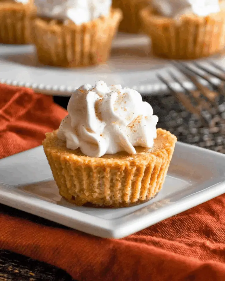 Mini keto pumpkin pie topped with a swirl of whipped cream and a sprinkle of cinnamon, served on a square white plate.