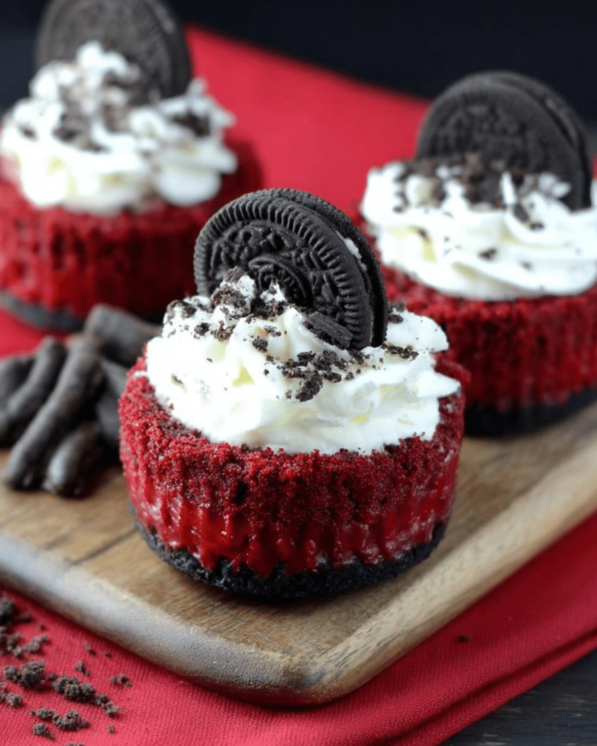 Mini Red Velvet Cheesecakes topped with whipped cream, crushed Oreo cookies, and whole Oreo cookies as garnish.