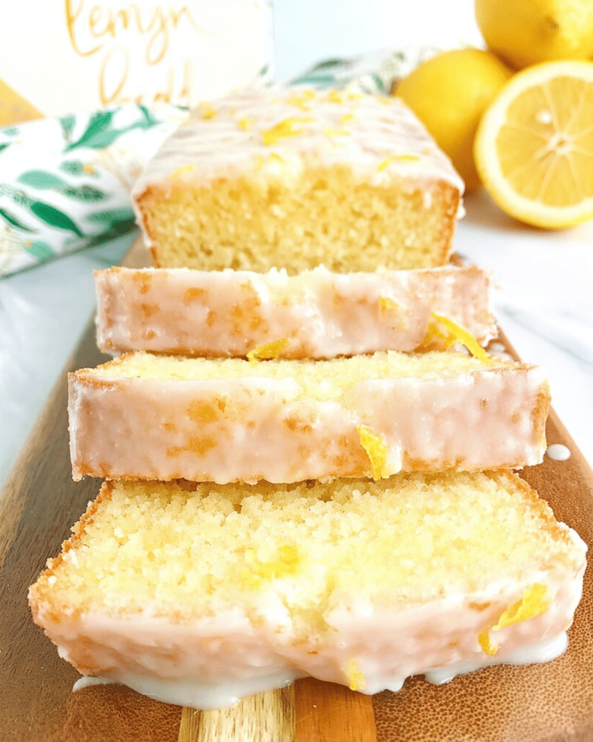 Moist lemon bread with glaze, sliced and served on a wooden board, garnished with lemon zest.