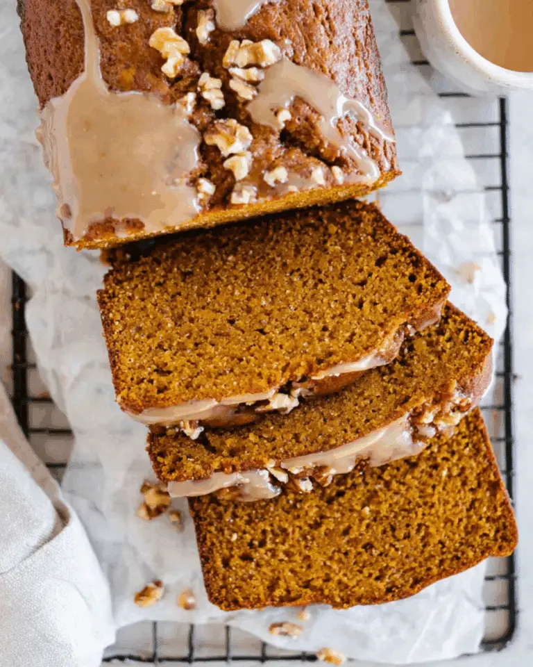 Sliced moist walnut pumpkin bread topped with glaze and chopped walnuts on a cooling rack.