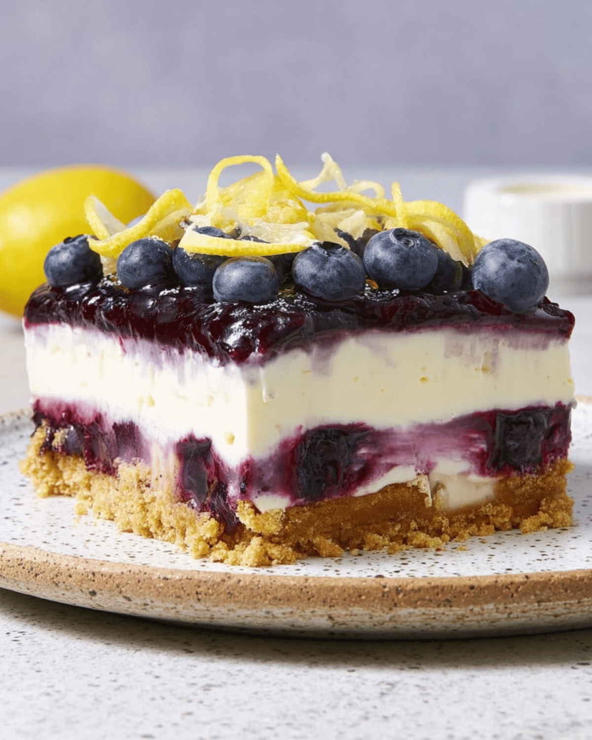 No-bake lemon blueberry delight dessert with a graham cracker crust, creamy lemon filling, blueberry layers, and fresh blueberries with lemon zest on top.