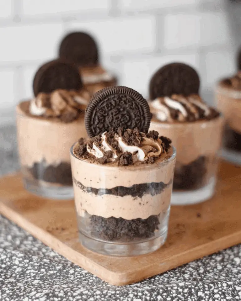 Individual no bake Oreo dessert cups layered with crushed Oreos, creamy filling, and topped with whipped cream and an Oreo cookie.