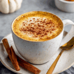 A cozy cup of coffee made with oatmilk pumpkin spice creamer, topped with cinnamon, with cinnamon sticks on the saucer.