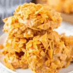 A stack of golden peanut butter cornflake cookies on a white plate, showing their crunchy texture.