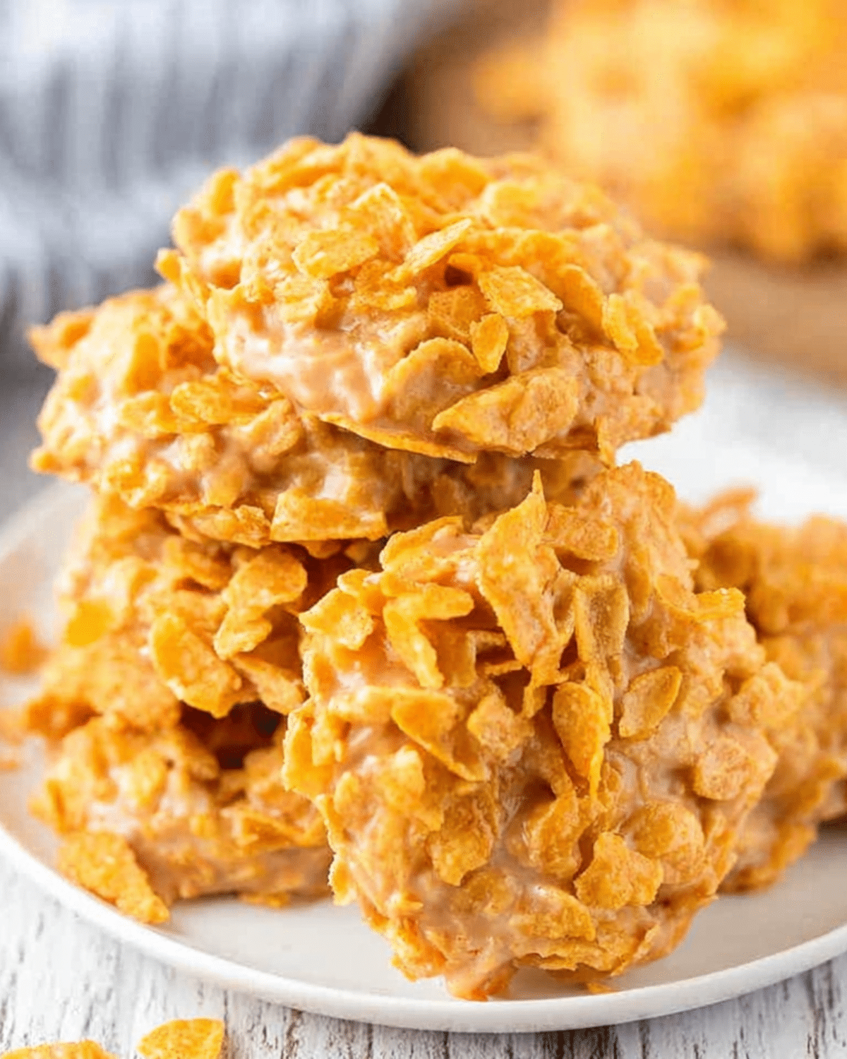 A stack of golden peanut butter cornflake cookies on a white plate, showing their crunchy texture.