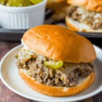A Philly cheesesteak sloppy joe sandwich on a soft bun, filled with seasoned ground beef, melted cheese, and pickle slices.