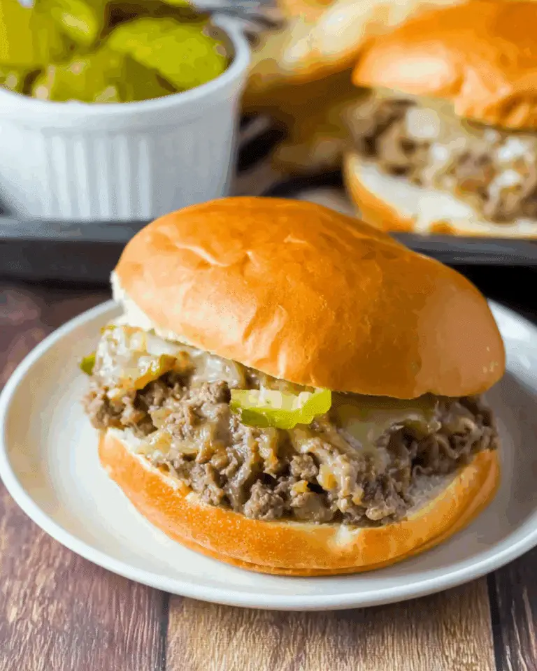A Philly cheesesteak sloppy joe sandwich on a soft bun, filled with seasoned ground beef, melted cheese, and pickle slices.