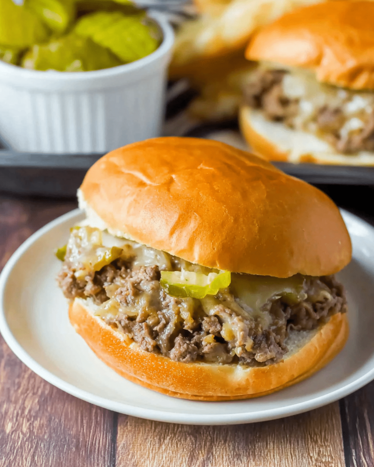 A Philly cheesesteak sloppy joe sandwich on a soft bun, filled with seasoned ground beef, melted cheese, and pickle slices.
