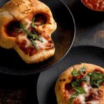 Pizza Skulls made with golden baked dough shaped like skulls, filled with marinara sauce, melted cheese, and fresh basil, served with a side of dipping sauce.