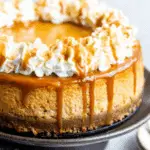 Pumpkin caramel cheesecake topped with whipped cream swirls and drizzled caramel sauce on a cake stand.