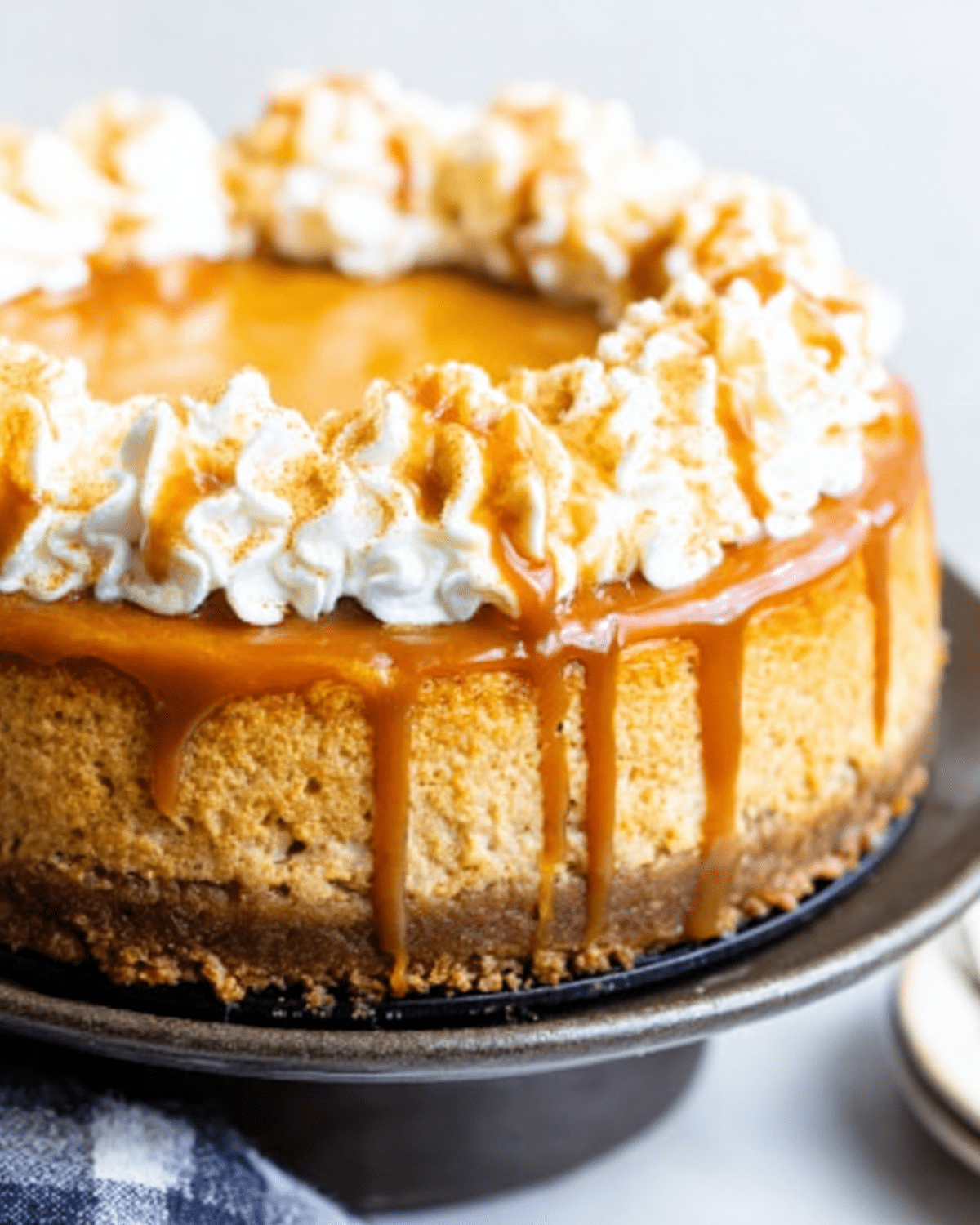 Pumpkin caramel cheesecake topped with whipped cream swirls and drizzled caramel sauce on a cake stand.