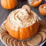 Bowl shaped like a pumpkin filled with pumpkin cheesecake dip, surrounded by gingersnap cookies.