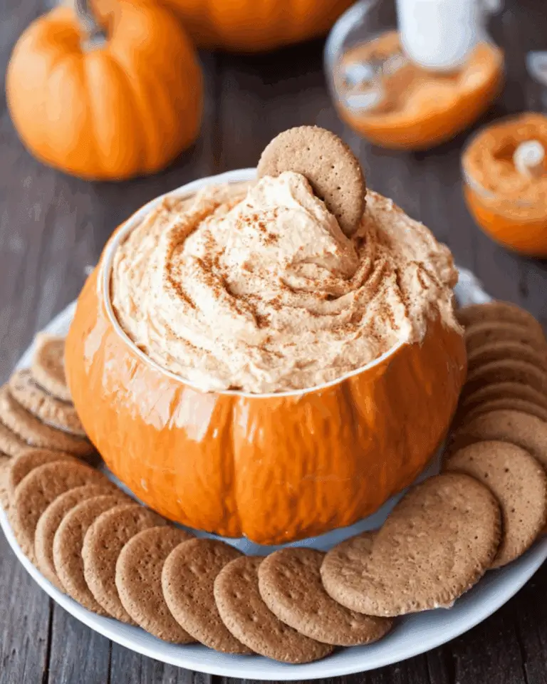 Bowl shaped like a pumpkin filled with pumpkin cheesecake dip, surrounded by gingersnap cookies.