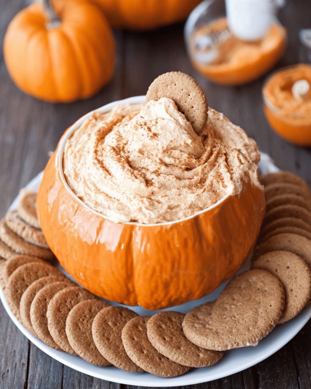 Bowl shaped like a pumpkin filled with pumpkin cheesecake dip, surrounded by gingersnap cookies.