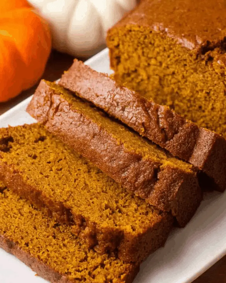 Sliced pumpkin loaf on a white plate, with whole pumpkins in the background.