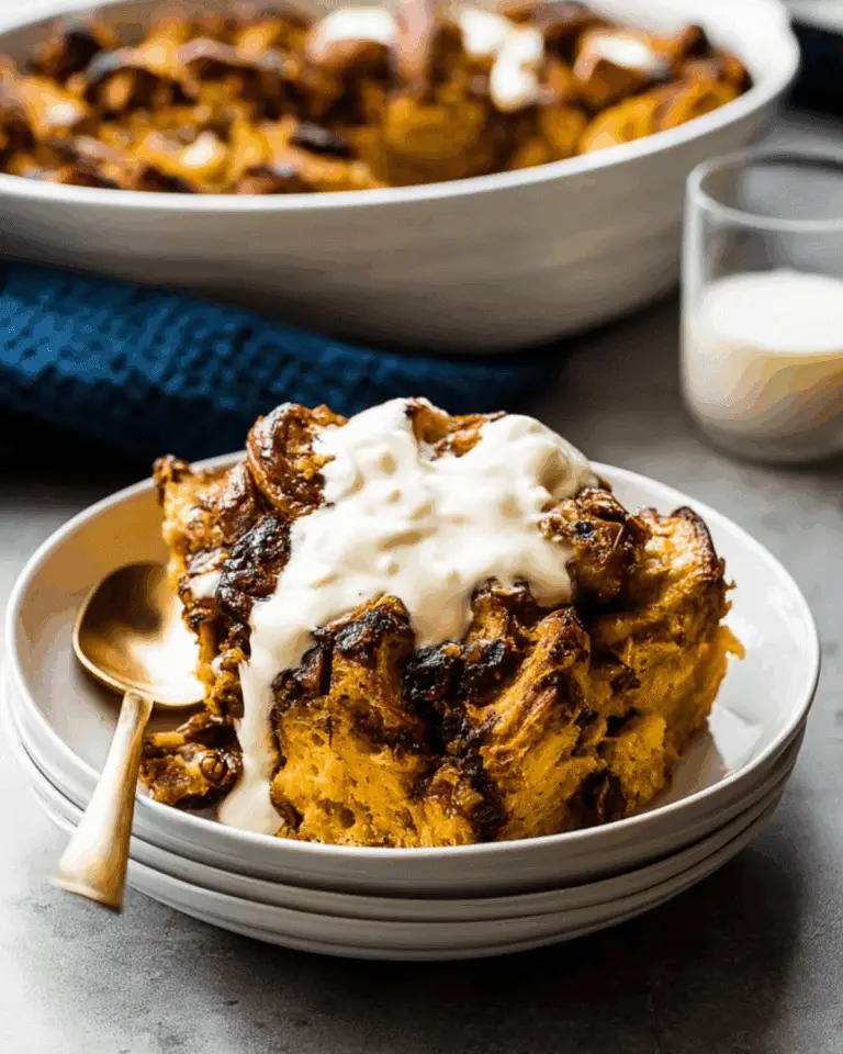 Pumpkin Pie Bread Pudding with Challah served in a bowl, topped with creamy sauce and a golden crust.