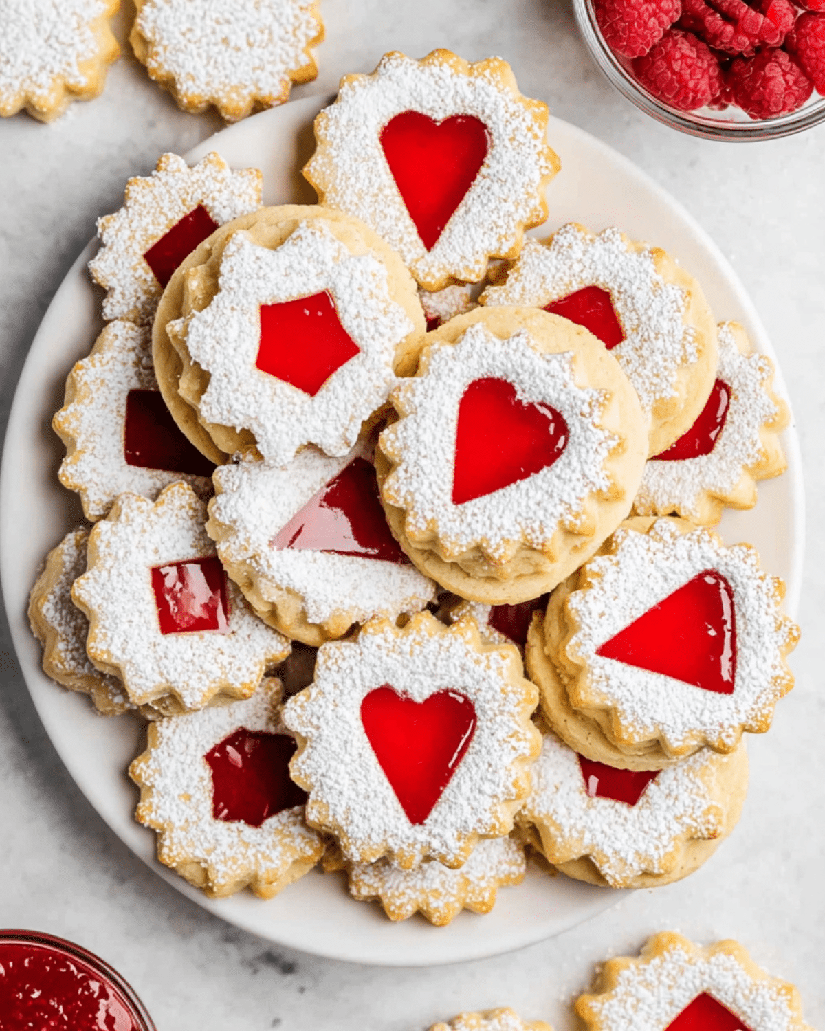 Raspberry Linzer cookies dusted with powdered sugar and filled with red raspberry jam in various cut-out shapes.