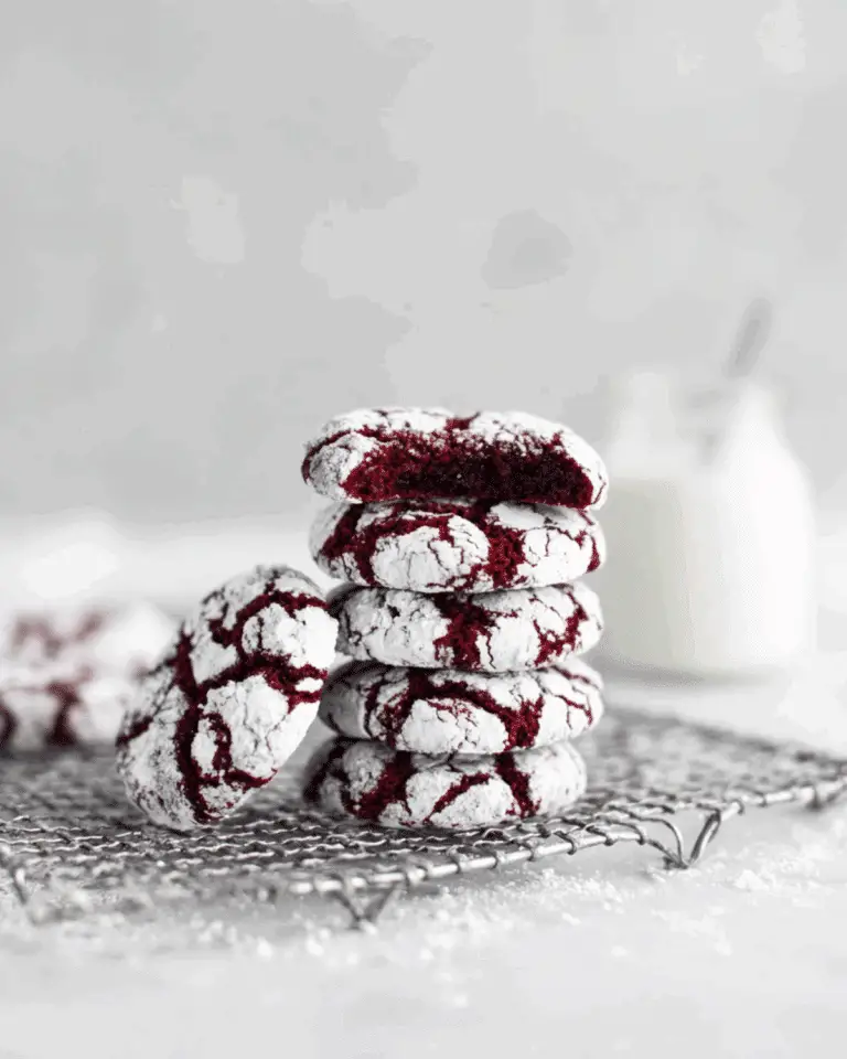 A stack of Red Velvet Crinkle Cookies coated in powdered sugar, with one cookie showing a soft, chewy interior.