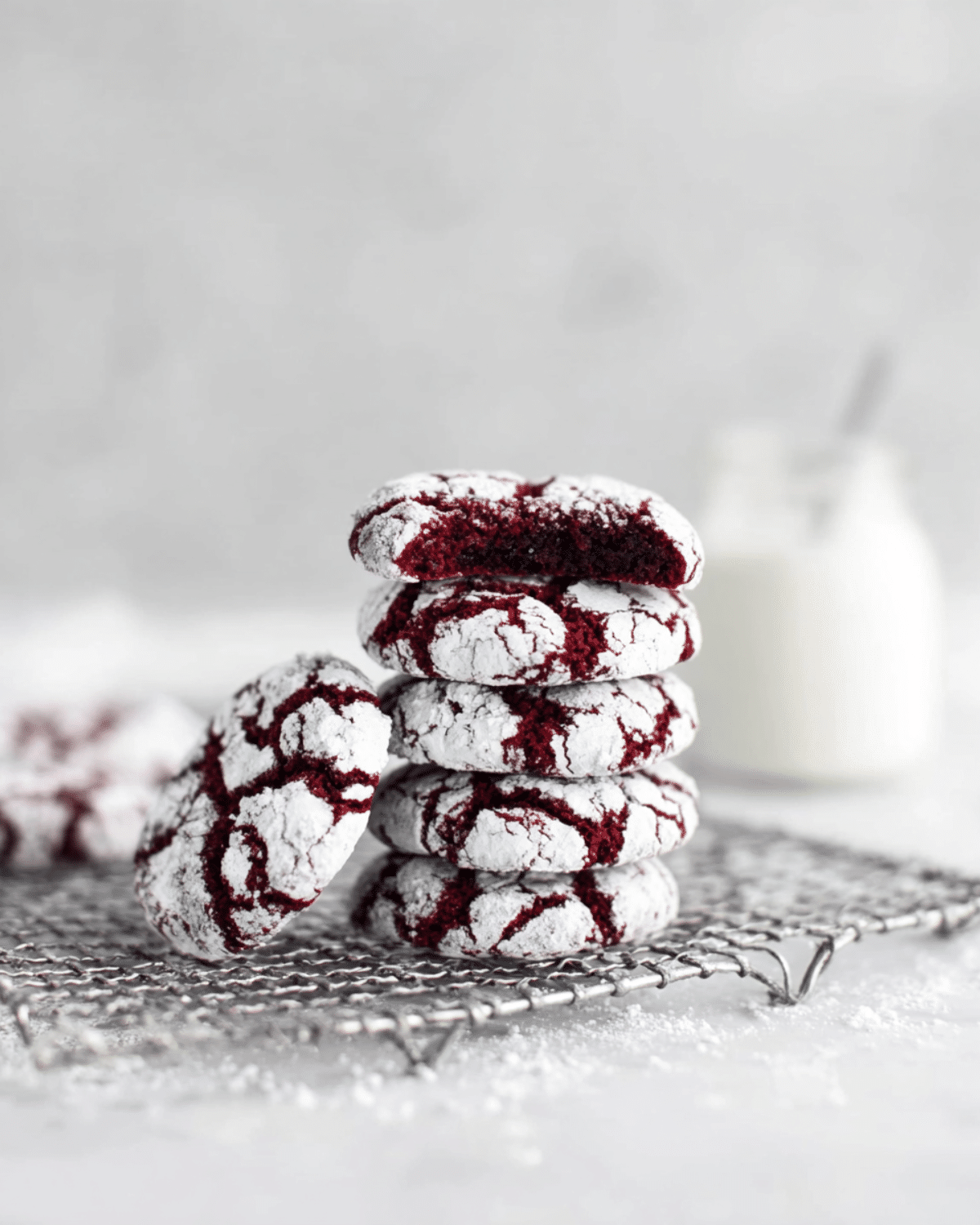 A stack of Red Velvet Crinkle Cookies coated in powdered sugar, with one cookie showing a soft, chewy interior.