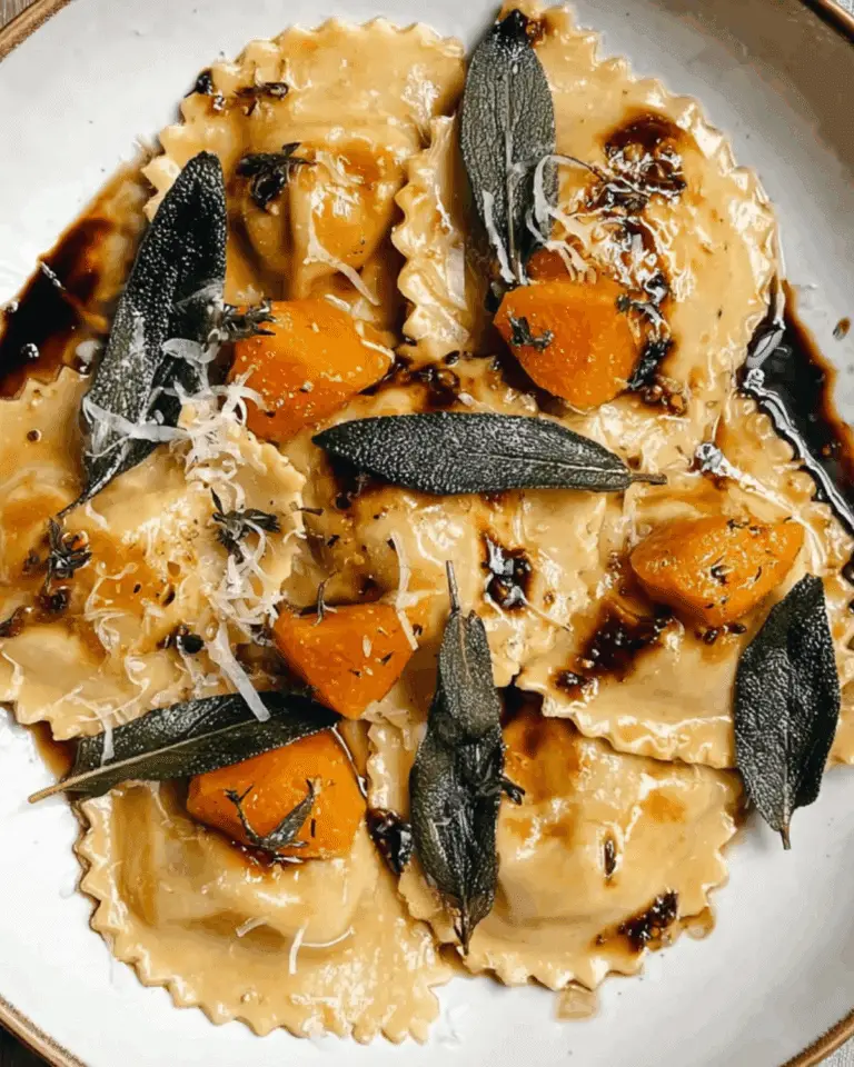Roast pumpkin agnolotti topped with crispy sage leaves, shaved parmesan, balsamic glaze, and chunks of roasted pumpkin on a white plate.