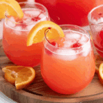 Glasses of Shirley Temple Punch with ice, cherries, and orange slices on a wooden tray.