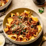 A bowl of slow cooked short rib ragu with pappardelle pasta, topped with grated cheese and fresh herbs.