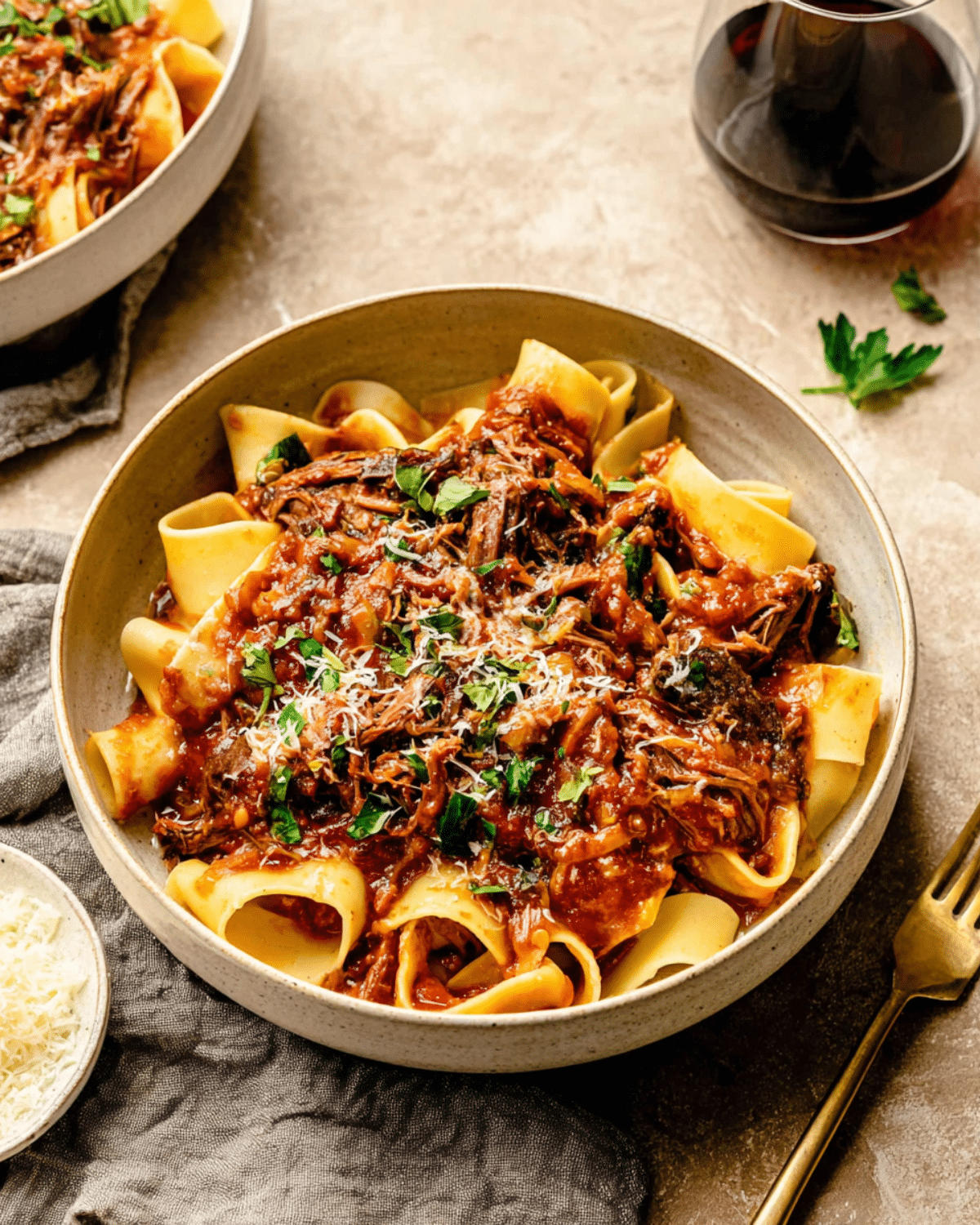 A bowl of slow cooked short rib ragu with pappardelle pasta, topped with grated cheese and fresh herbs.
