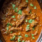 Slow cooker beef curry with tender beef chunks in a rich red curry sauce, garnished with fresh cilantro.