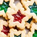 Stained glass cookies with red and green candy centers shaped like stars, dusted with powdered sugar.