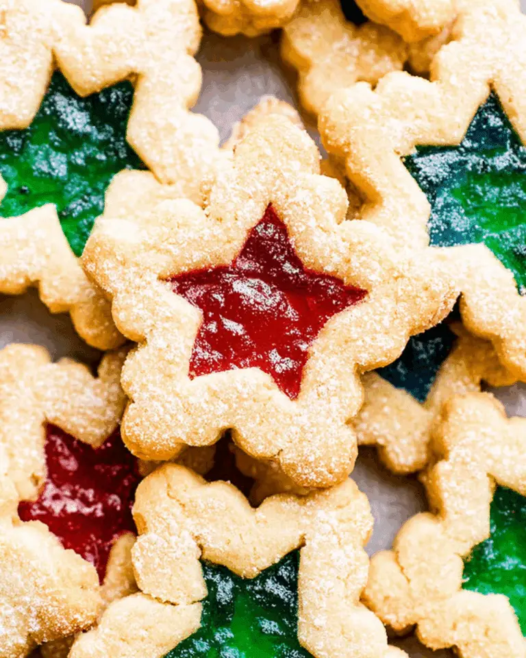 Stained glass cookies with red and green candy centers shaped like stars, dusted with powdered sugar.